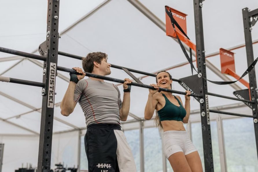 Man and woman exercising with pull-ups in an indoor gym, showcasing fitness and strength.